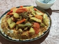 A vibrant plate of Moroccan couscous topped with colorful vegetables, chickpeas, and tender pieces of lamb, served with a side of spicy harissa sauce.