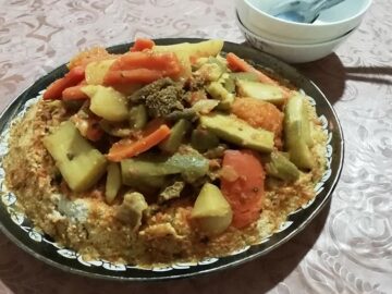 A vibrant plate of Moroccan couscous topped with colorful vegetables, chickpeas, and tender pieces of lamb, served with a side of spicy harissa sauce.