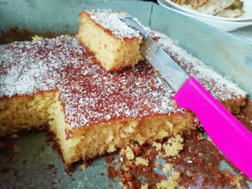 A homemade coconut cake with layers of creamy frosting and a generous sprinkle of shredded coconut, served on a rustic wooden table.